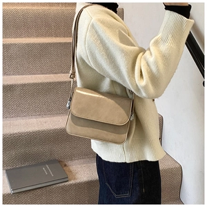 Khaki square shoulder bag with silver buckle worn by a model in a warm setting