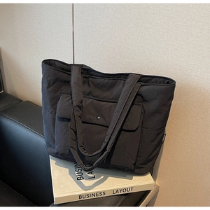 Detail of black quilted tote bag with wide shoulder straps and front snap flap pocket