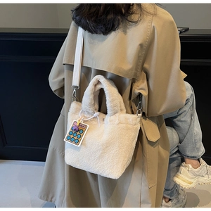 Detail view of cream plush bucket bag with a yellow calculator charm on a trench coat