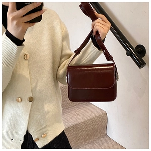 Burgundy glossy crossbody bag shown on model with adjustable strap and casual style