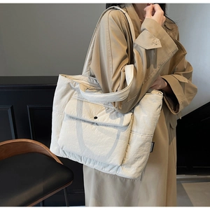 Detail of a large beige nylon tote bag with a front snap pocket and woven brand label
