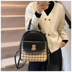 Close-up of a women's black leather backpack with brown plaid detail and bear embroidery