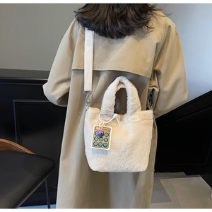 Detail of plush bucket bag in creamy white with wide canvas strap and cute calculator charm