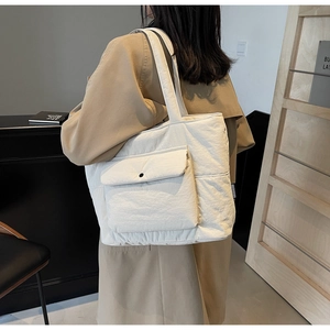 Detail of a beige quilted tote bag showing the snap button pocket and soft fabric texture