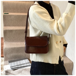 Model showing a deep red glossy leather flap crossbody bag on a bright staircase
