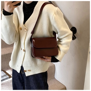 Detail of burgundy patent leather square shoulder bag with adjustable strap on a model