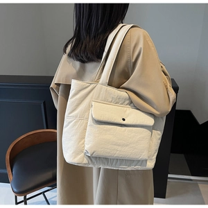 Detail of cream quilted tote bag with front snap pocket shown on a model's shoulder