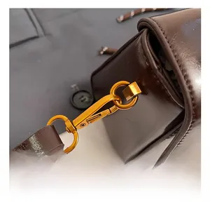 Detail showing high-quality golden metal hook and textured brown leather on a crossbody bag