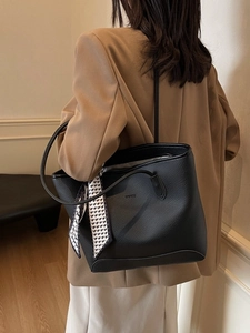 Fashionable black pebbled leather tote bag with silk scarf on a model in a minimalist setting