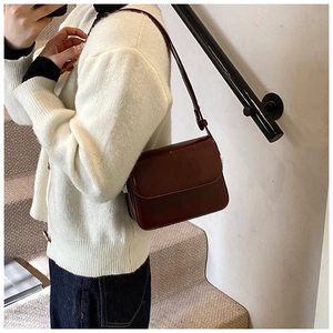 Side view of a dark reddish-brown leather crossbody bag worn by a model in casual attire