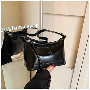 Detail of black glossy pillow bag featuring gold metal logo and adjustable strap