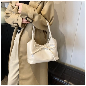 Gros plan d'un sac à bandoulière crème avec nœud porté avec un trench-coat classique