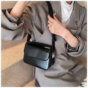 Close-up of minimalist black square shoulder bag in glossy faux leather with silver buckle
