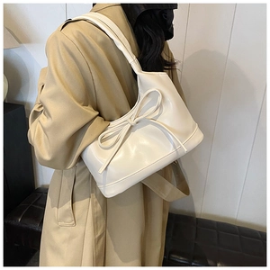 Sac à bandoulière beige chic avec grand nœud porté par un mannequin en trench-coat