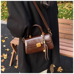 Detail der kaffeebraunen Lederhandtasche mit Goldverschluss und Anhängern auf einer Parkbank