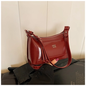 Detail view of burgundy patent leather crescent bag featuring golden logo and glossy finish