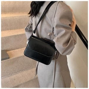 Detail of a black patent leather crossbody bag showing adjustable strap and metal hardware