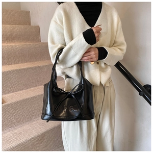 Détail d'un sac à main en cuir noir avec lettres embossées et nœud décoratif