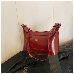 Detail of red glossy patent leather shoulder bag with gold metal logo and sleek strap