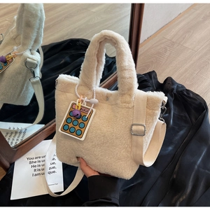 Detail of beige plush bucket bag with fuzzy texture, ribbon strap and calculator charm