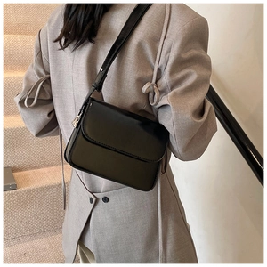 Chic black glossy leather crossbody bag shown on a model with minimalist metal hardware