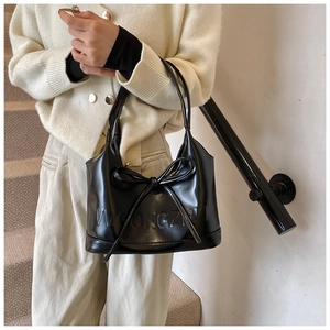 Détail du sac bandoulière noir brillant avec nœud et gaufrage porté par un modèle