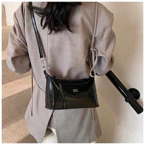 Detail of a black patent leather crossbody bag with silver COIN logo on a brown blazer