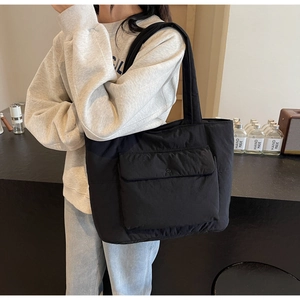 Side view of a large black quilted tote bag with a snap pocket on a female model