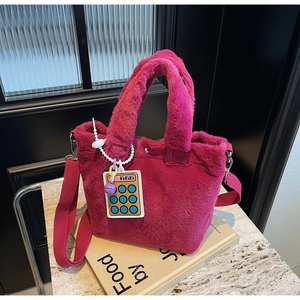 Close-up of bright magenta plush bucket bag with wide strap and calculator charm