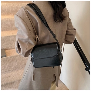 Fashionable black glossy square crossbody bag shown on a model in an urban setting