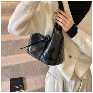 Détail d'un sac à main en cuir noir mat avec lettres embossées et un nœud décoratif en cuir