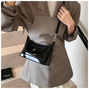 Detail of black glossy pillow bag with silver hardware on gray suit model