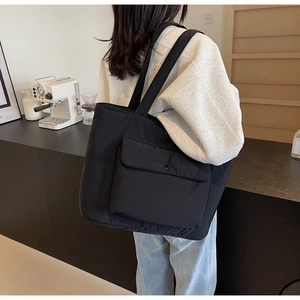 Minimalist black quilted tote bag with front pocket shown in a lifestyle daily setting