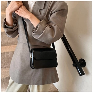 Minimalist black glossy leather square crossbody bag worn by a model on stairs
