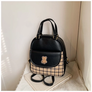 Detail of minimalist backpack showing bear patch and plaid fabric base on white prop