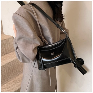 Detailed view of the black glossy leather shoulder bag worn by a model in a minimal setting