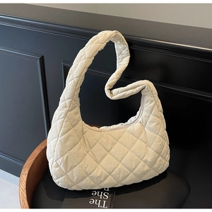 Close-up of cream quilted hobo bag with diamond pattern on a dark wood stand