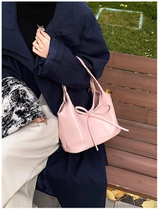 Sac à main rose en similicuir avec un nœud décoratif posé sur un banc de parc