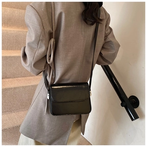Minimalist black square crossbody bag shown on model in a modern staircase setting
