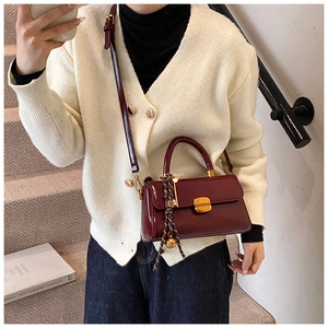 Detail einer burgunderroten glänzenden Handtasche mit Goldschnalle und Seidenschal
