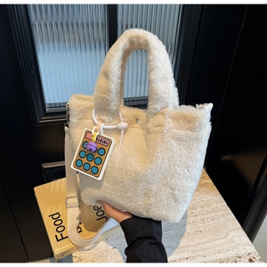 Detail of plush off-white bucket bag with a funny calculator charm and canvas strap