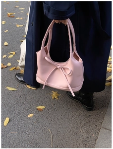 Sac à main rose minimaliste avec nœud tenu par un mannequin sur une rue d'automne