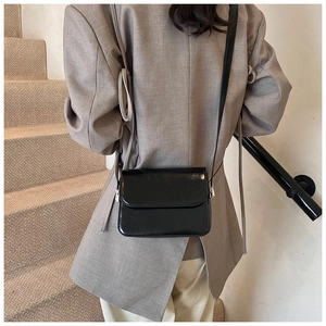 Polished black crossbody bag shown on a person for scale in a minimalist setting