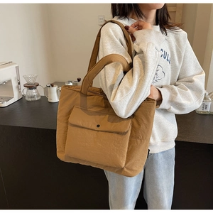 Close-up of khaki quilted tote bag featuring a snap-button front pocket in a cafe setting