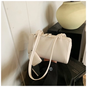Detail view of cream rectangle underarm bag with decorative charm and dual metal zippers