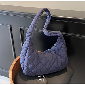 Close-up of dark blue quilted puffer bag with glossy finish and soft padded shoulder strap