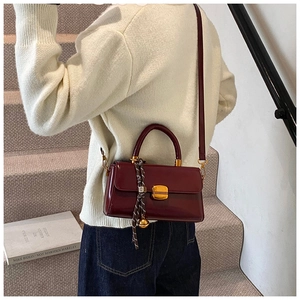 Detail of burgundy leather handbag with gold square lock and silk scarf wrapped handle