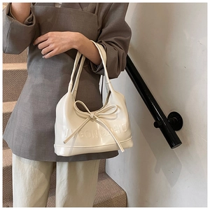 Détail du sac à bandoulière crème en cuir verni avec nœud et lettrage en relief