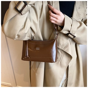Detail of glossy brown leather shoulder bag with silver metal logo and precise stitching
