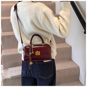 Close-up of burgundy patent leather handbag with gold square buckle on a staircase